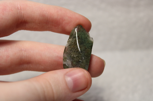Polished clear stone with green clusters inside.